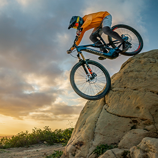 Mountain biker wearing Anetik performance apparel riding along a coastal trail with ocean backdrop